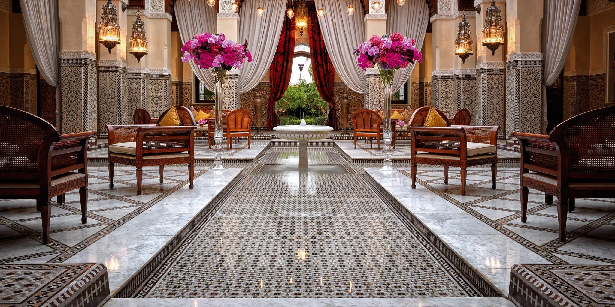 Elegant interior of Royal Mansour in Marrakesh featuring detailed mosaic floors, richly upholstered seating, and draped curtains.