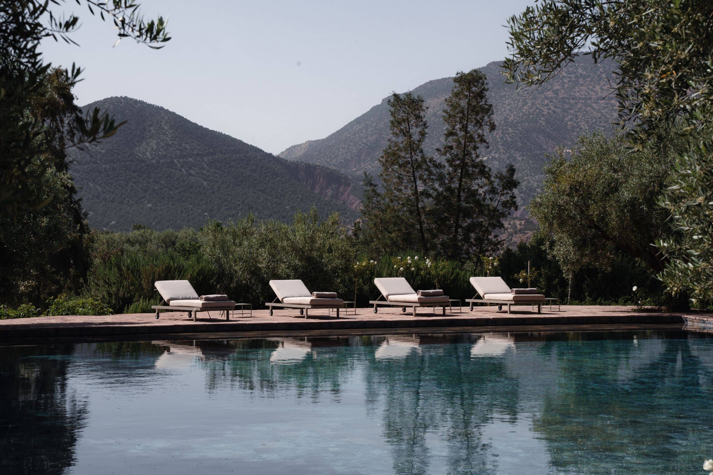 An idyllic scene at the Olinto Atlas Mountain Retreat, with sun loungers perfectly positioned beside a tranquil pool that reflects the clear mountain sky.