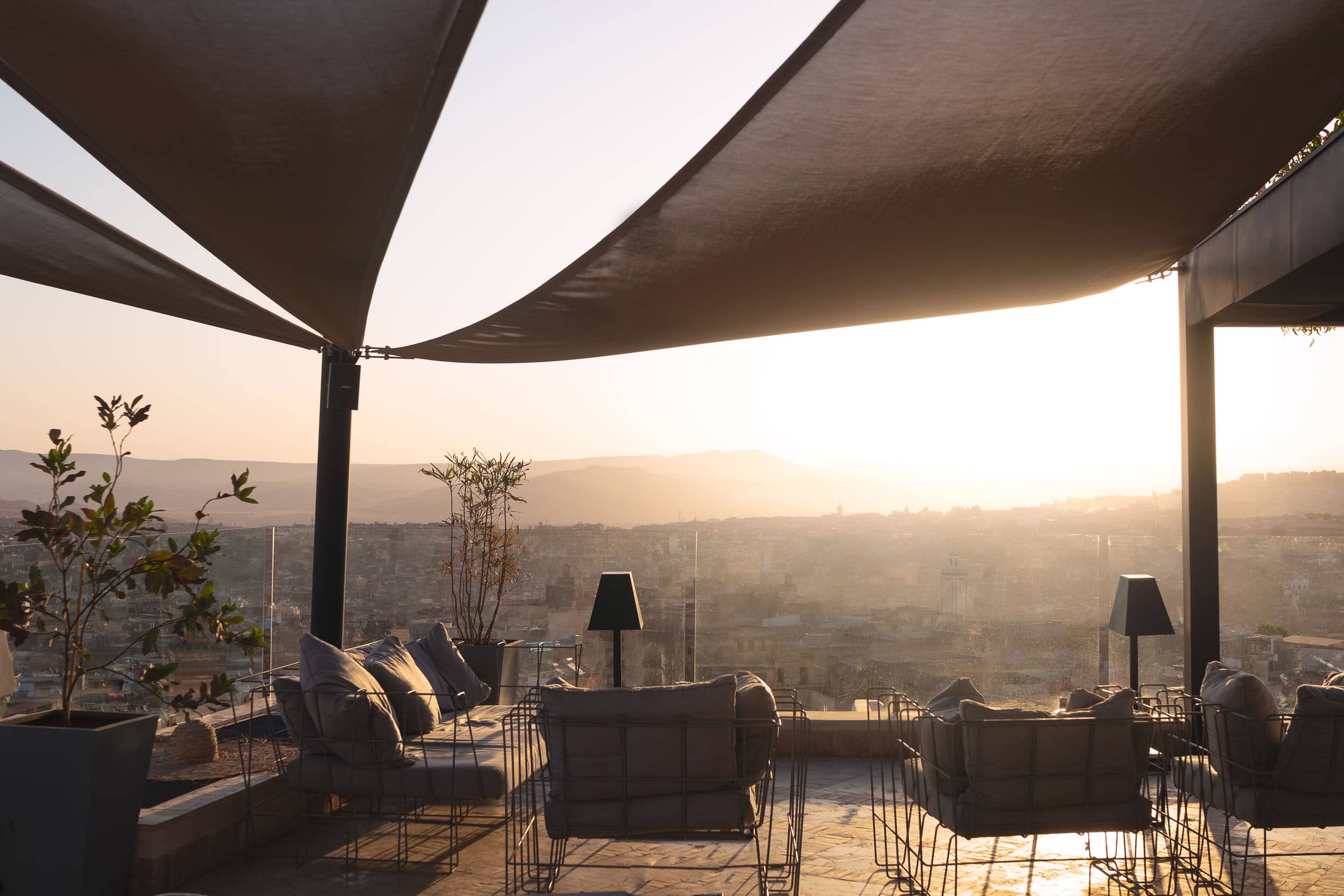 A serene and picturesque rooftop lounge at Riad Fes, offering breathtaking views of the cityscape at sunset, with comfortable seating and elegant decor.