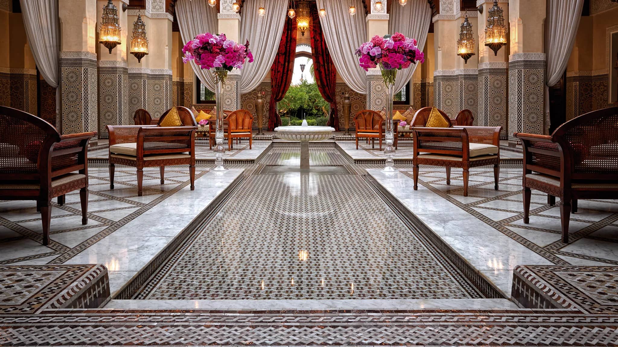 A luxurious lounge area in Royal Mansour, adorned with intricate tilework, elegant furnishings, and vibrant floral arrangements, exemplifying Moroccan opulence and design.