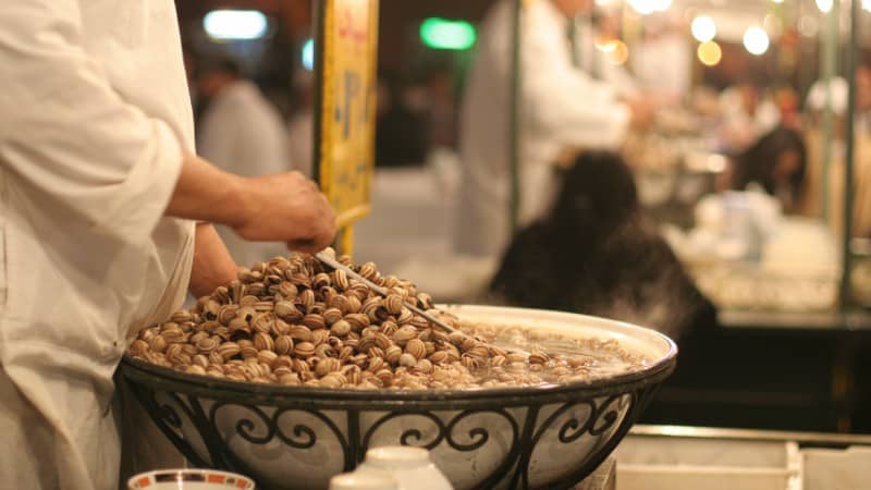 A street food vendor in Morocco serving a popular dish of 'boubouche' (snails), cooked in a flavorful broth and served hot to eager customers.