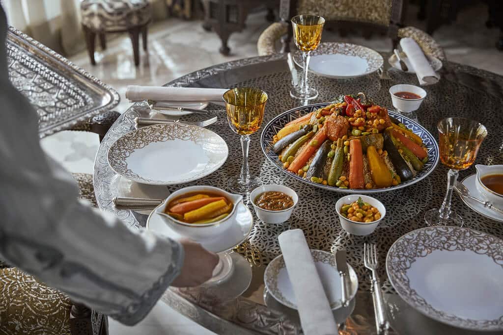 A traditional Moroccan meal served in the luxurious setting of Royal Mansour, showcasing a beautifully arranged couscous dish with colorful vegetables and elegant tableware.