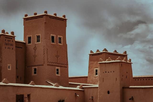 Traditional clay buildings with intricate designs under a cloudy sky in Morocco.