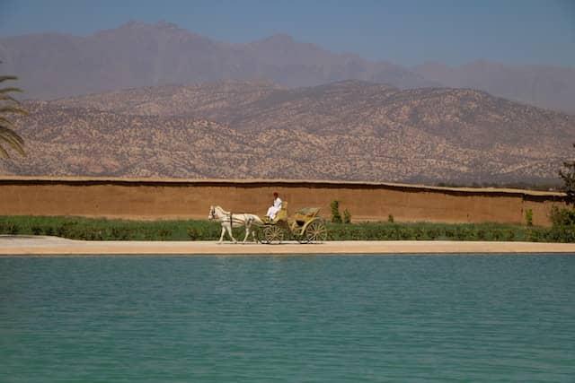 A horse-drawn carriage passing by the Menara Water reservoir with a backdrop of mountains in Marrakesh, Morocco.