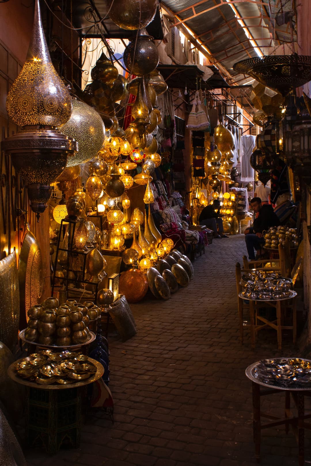 Cover of a travel guide about Ramadan, featuring a vibrant marketplace with brass lamps and lanterns illuminating a narrow cobblestone alley, showcasing Moroccan cultural heritage.